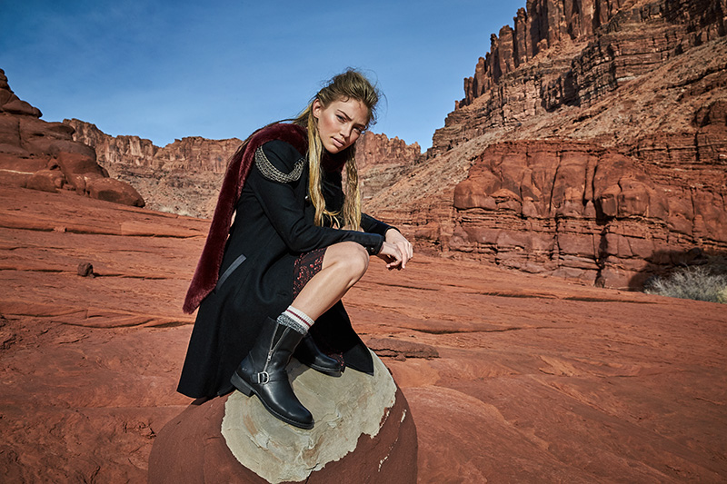 woman wearing vintage military coat perched on a boulder
